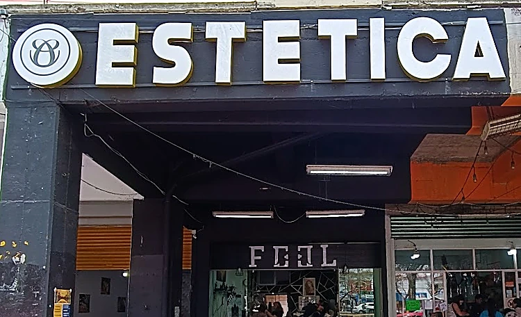 Entrada del pasillo comercial con el letrero ESTETICA en letras blancas sobre negro y el sello redondo; al fondo del pasillo, el letrero FEEL