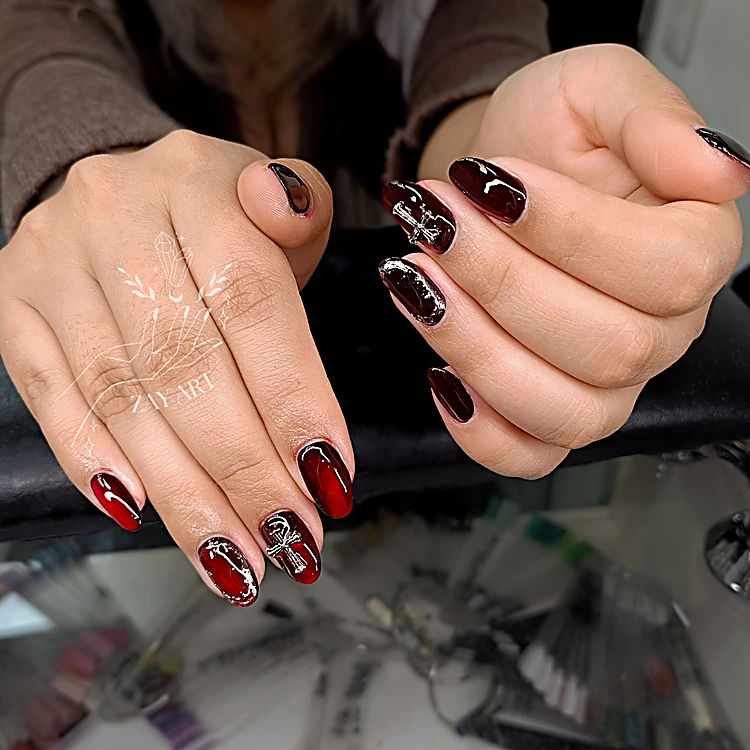 Uñas en guinda translúcido con una cruz plateada, apoyadas en el banco negro